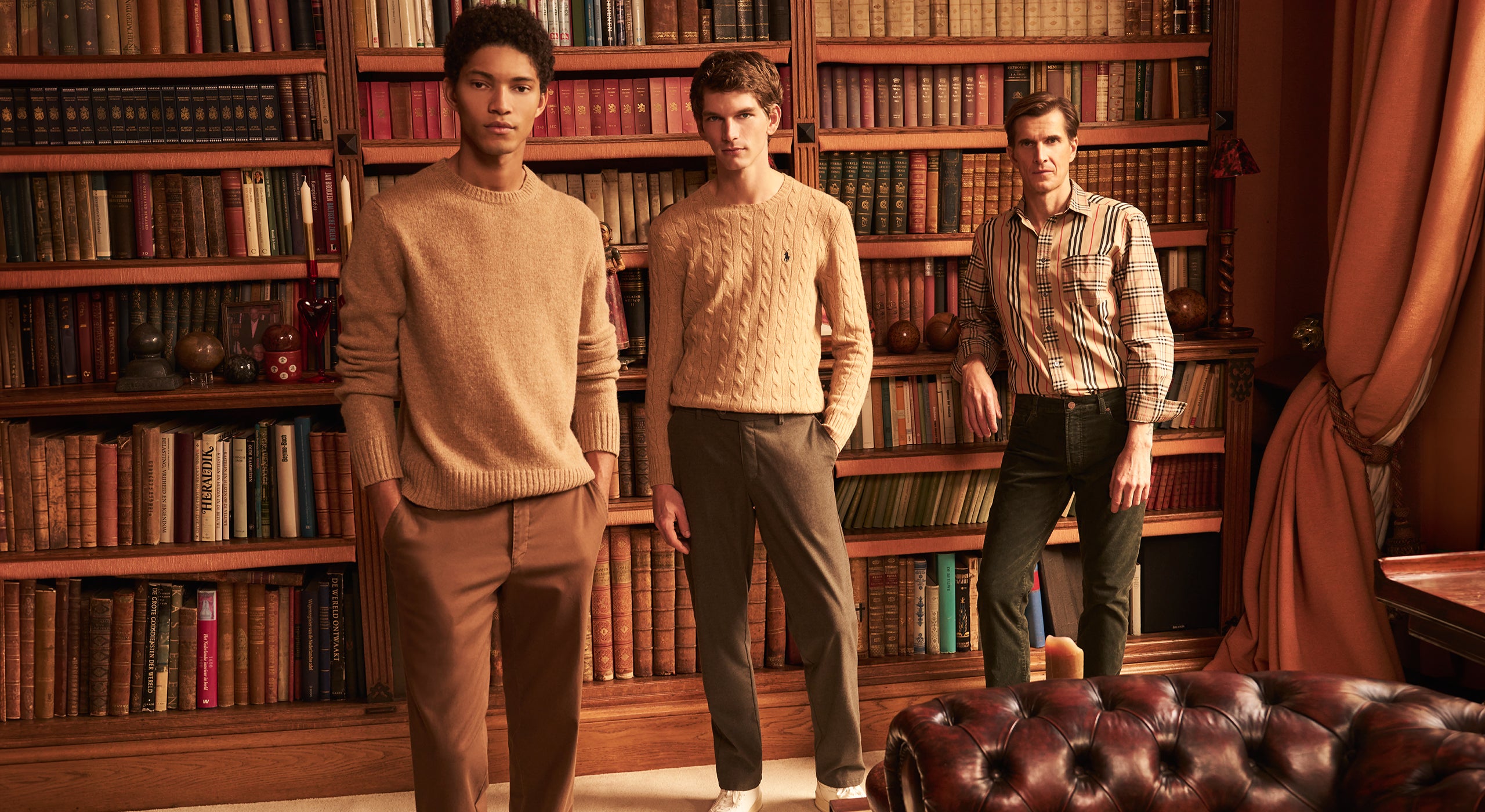 Three men standing in a room with bookshelves and a leather chair.