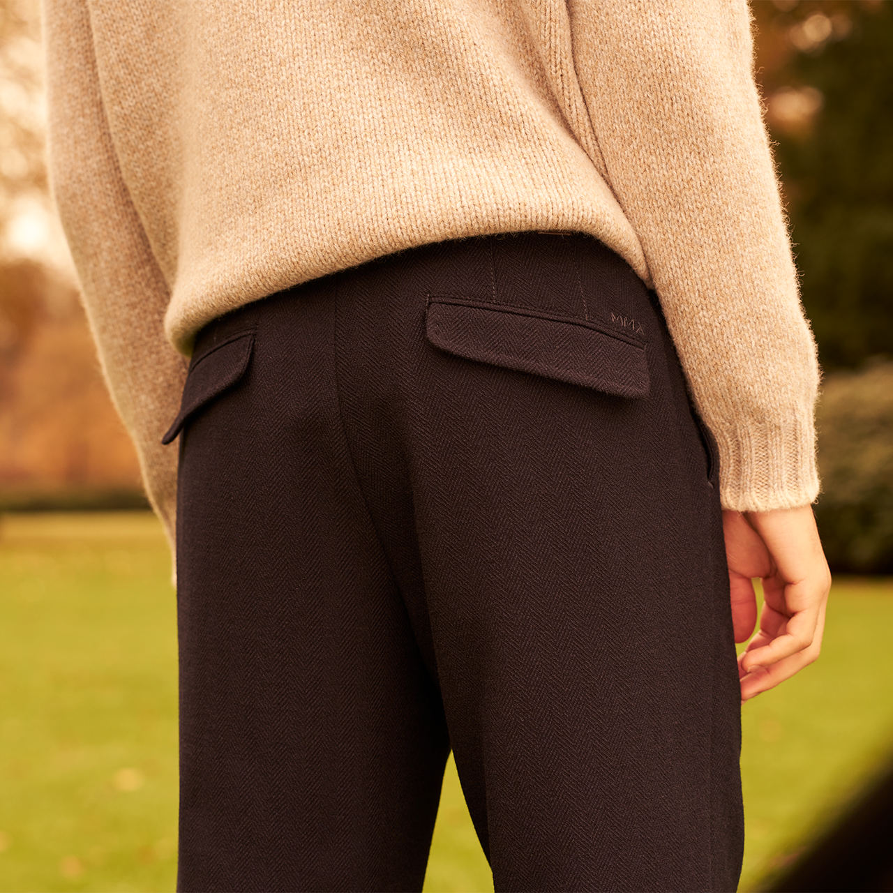 Person wearing dark pants and a beige sweater outdoors